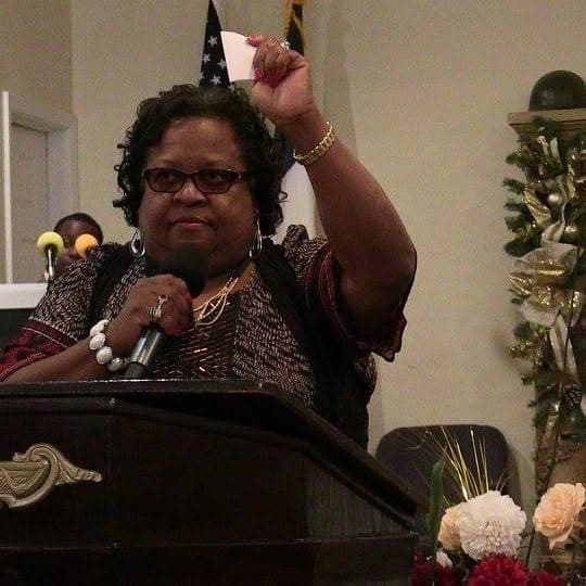 Apostle Allice Hood preaching at the pulpit at Christ Family Church, microphone in hand.