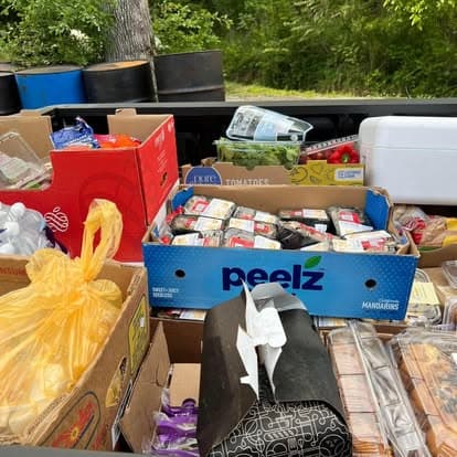 Boxes of groceries laid out for the food ministry: fresh produce, packs of meat, tomatoes, bread and full yellow grocery bags.